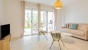 Una sala de estar moderna con un sofá, dos sillones, un televisor y una lámpara colgante amarilla.