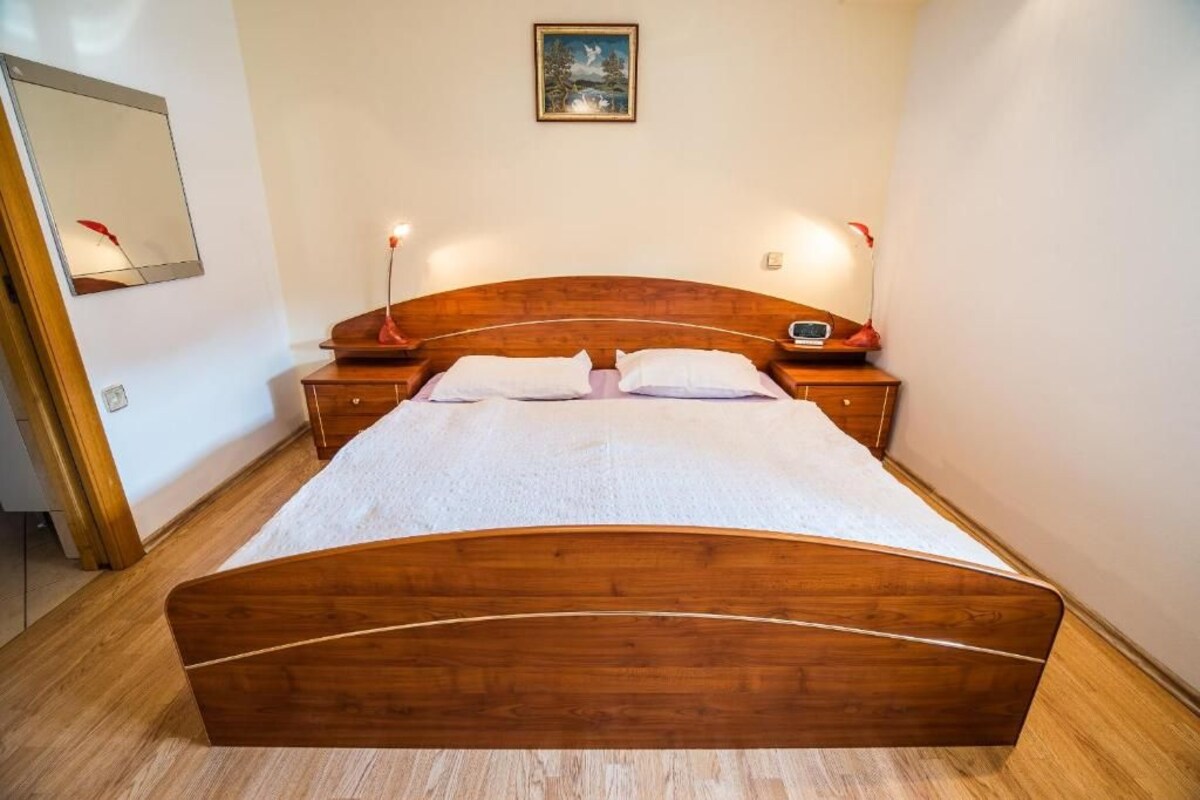 A wooden bed with two bedside tables, a nightstand, and a painting on the wall.
