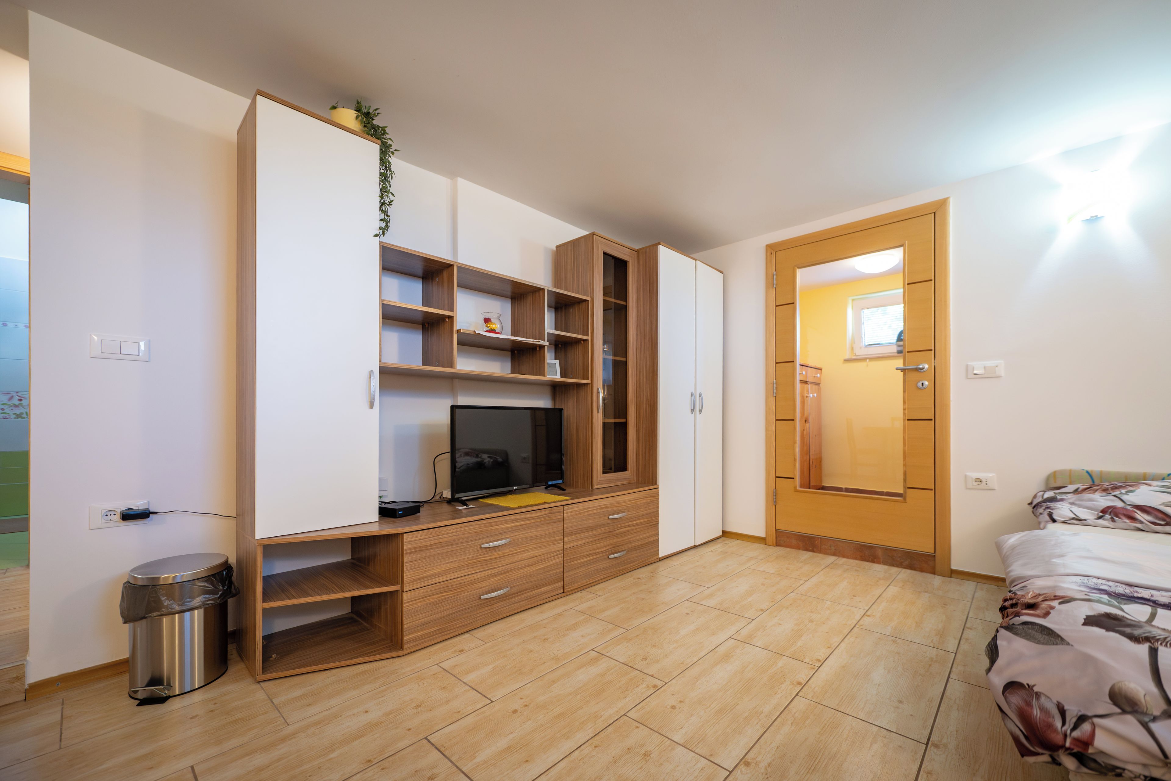 Ein Schlafzimmer mit einem Bett, einem Fernseher, einem Kleiderschrank und einem Papierkorb.