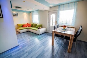 A modern living room with a sectional sofa, a dining table with chairs, and a large window with curtains. - Farm Stay Ana (Ivancna Gorica)