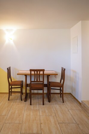 A dining area with a wooden table and chairs, a light fixture on the wall, and a door. - Farm Stay Ana (Ivancna Gorica)