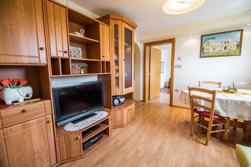 A wooden entertainment unit with a flat-screen TV, a dining table with chairs, and a painting on the wall.
