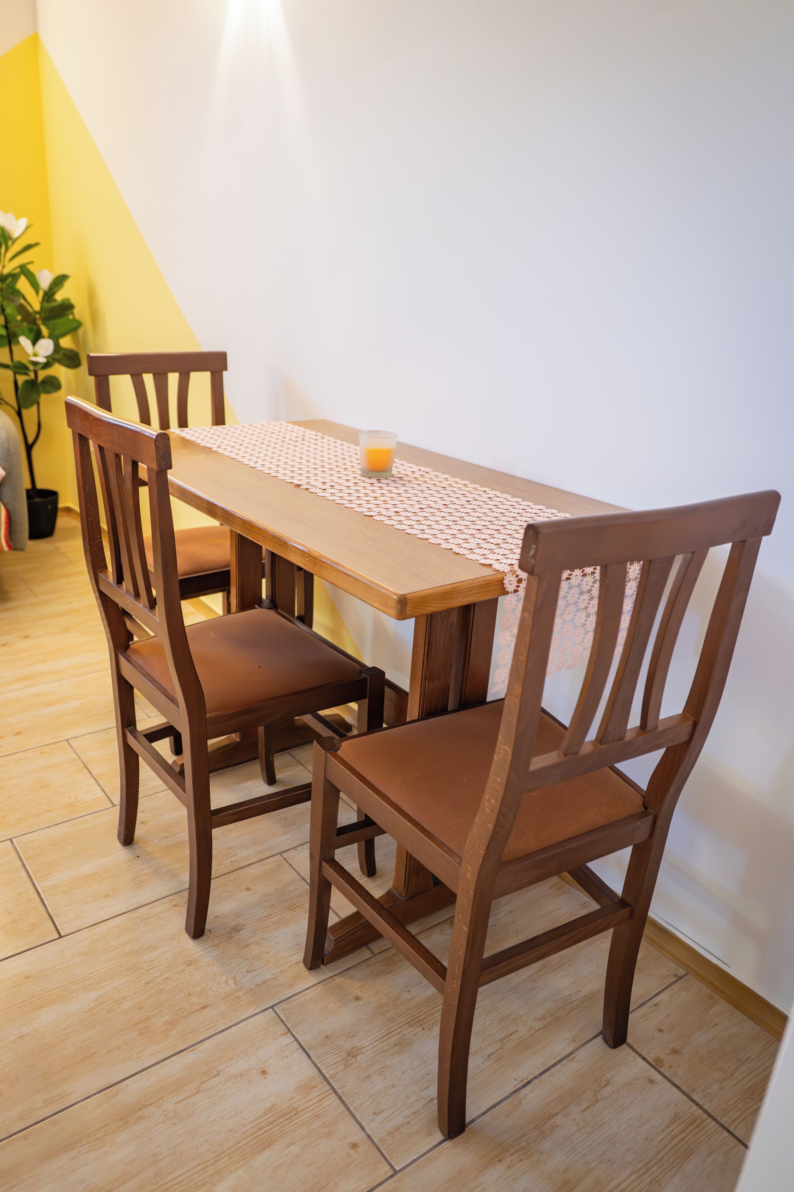 Ein Esstisch mit vier Holzstühlen, einer weißen Tischdecke mit Spitzenmuster und einem Glas Orangensaft.
