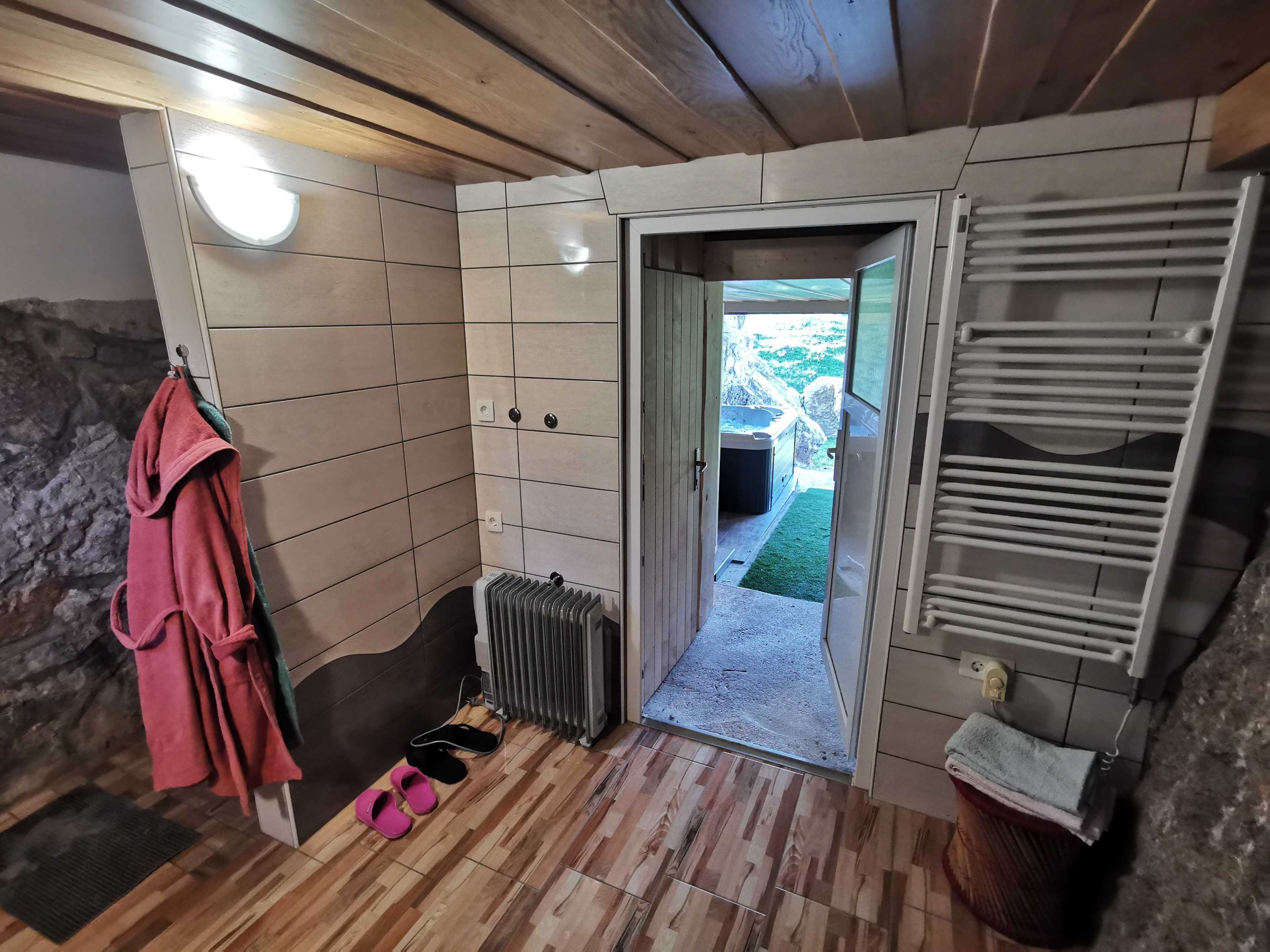 Un baño con techo de madera, un radiador, un perchero con una toalla, un par de pantuflas y una puerta abierta que da a un balcón.
