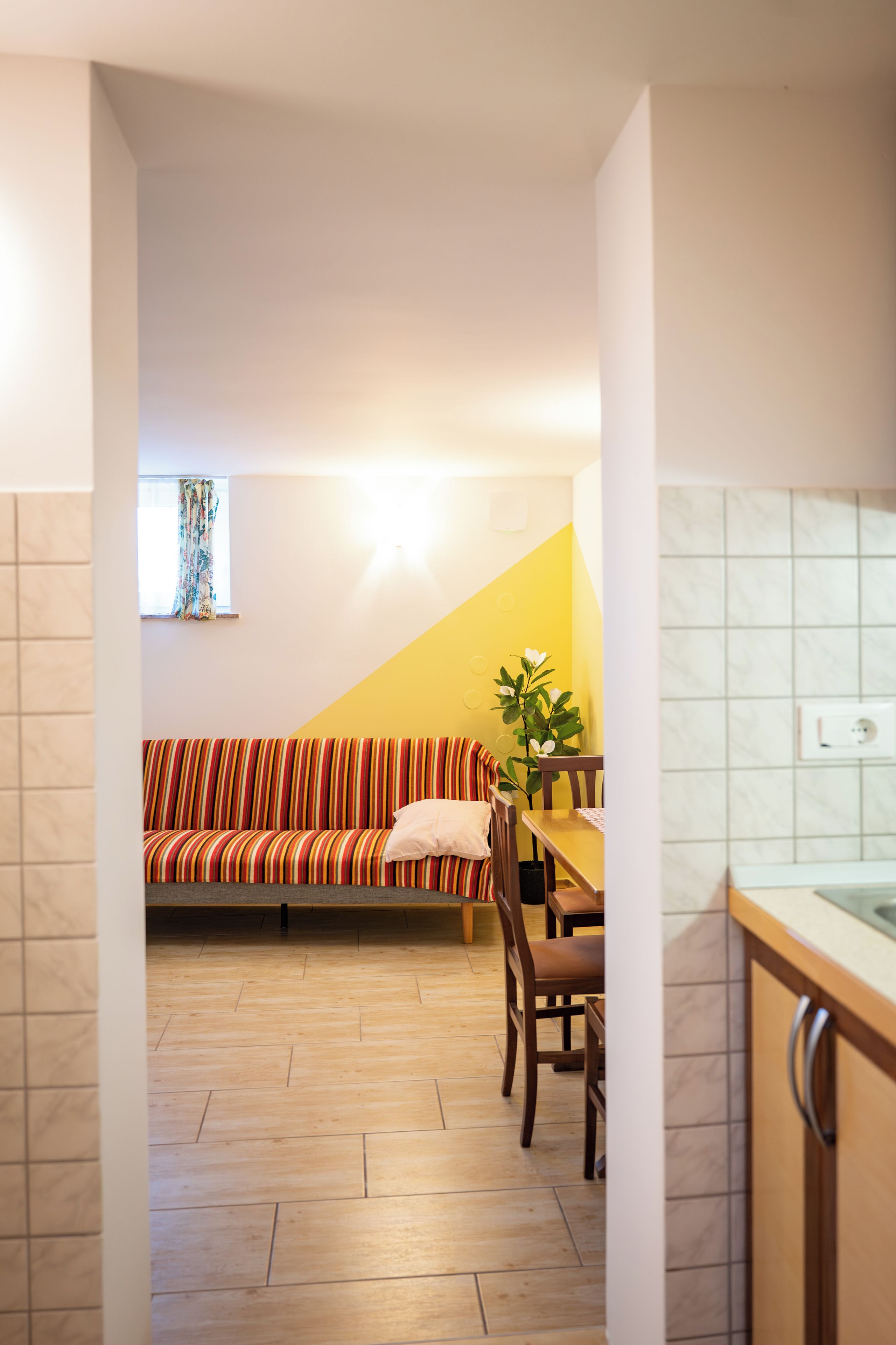 Un interior moderno con piso de madera, un sofá a rayas, una mesa de comedor con sillas y una zona de cocina con fregadero.