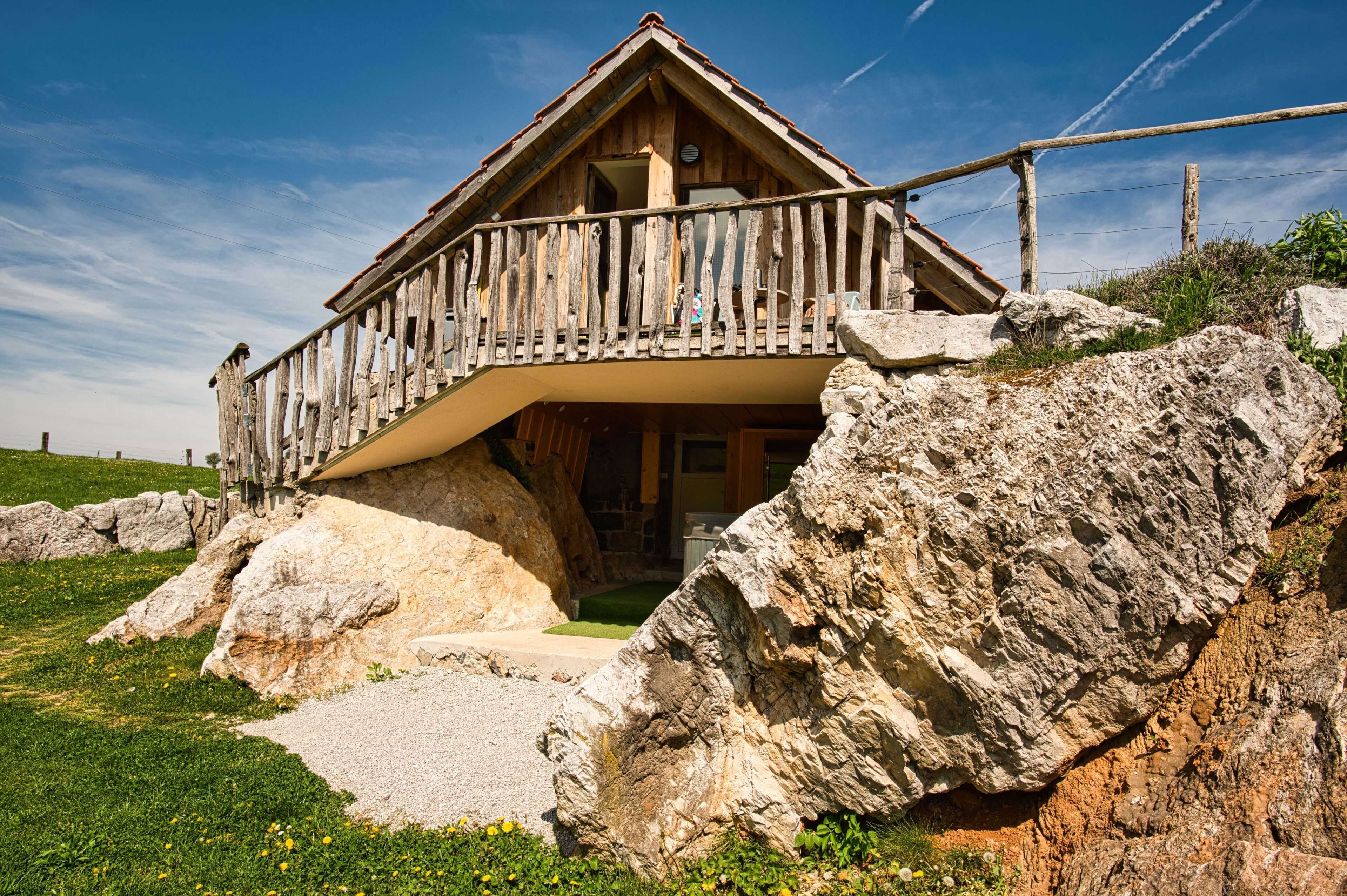 A wooden chalet with a balcony, set against a rocky hillside.