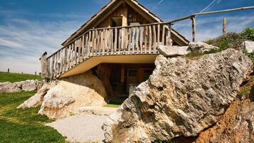 A wooden chalet with a balcony, set against a rocky hillside.