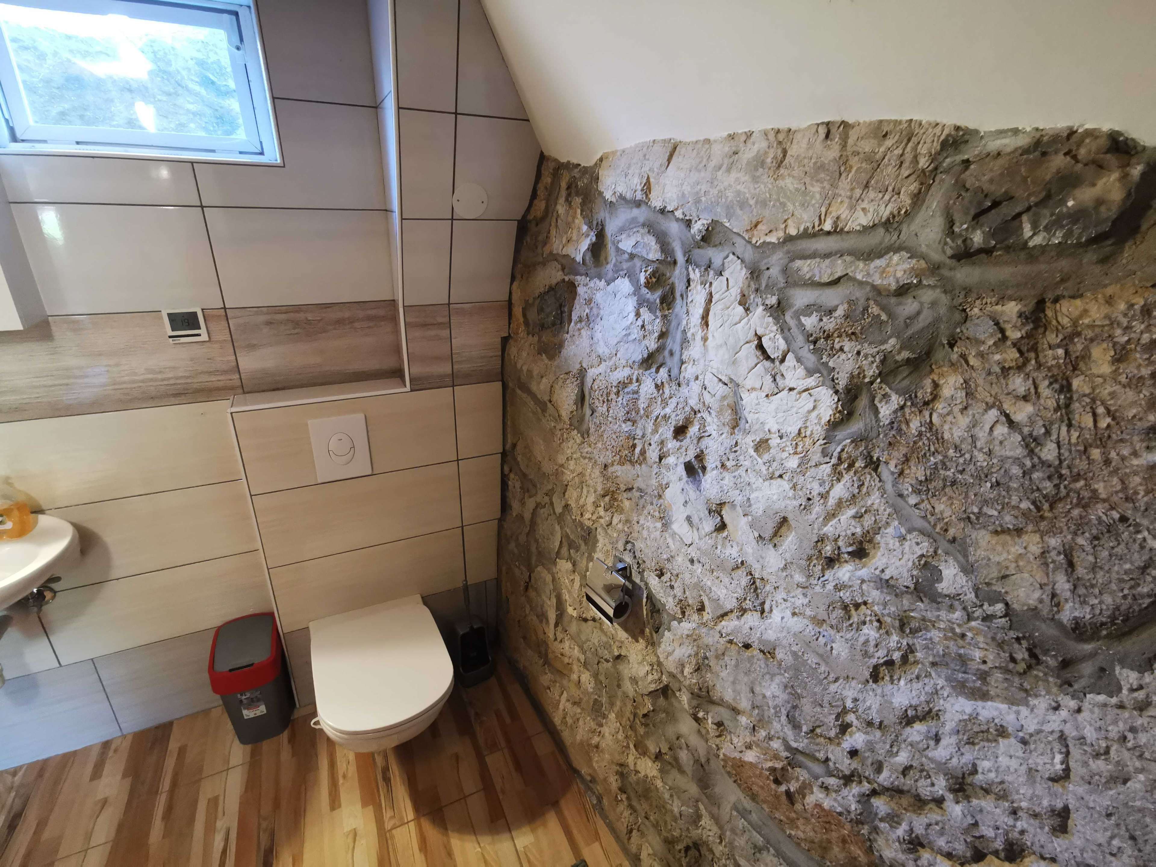 Une salle de bain avec un mur en pierre, des toilettes, un lavabo et une fenêtre.