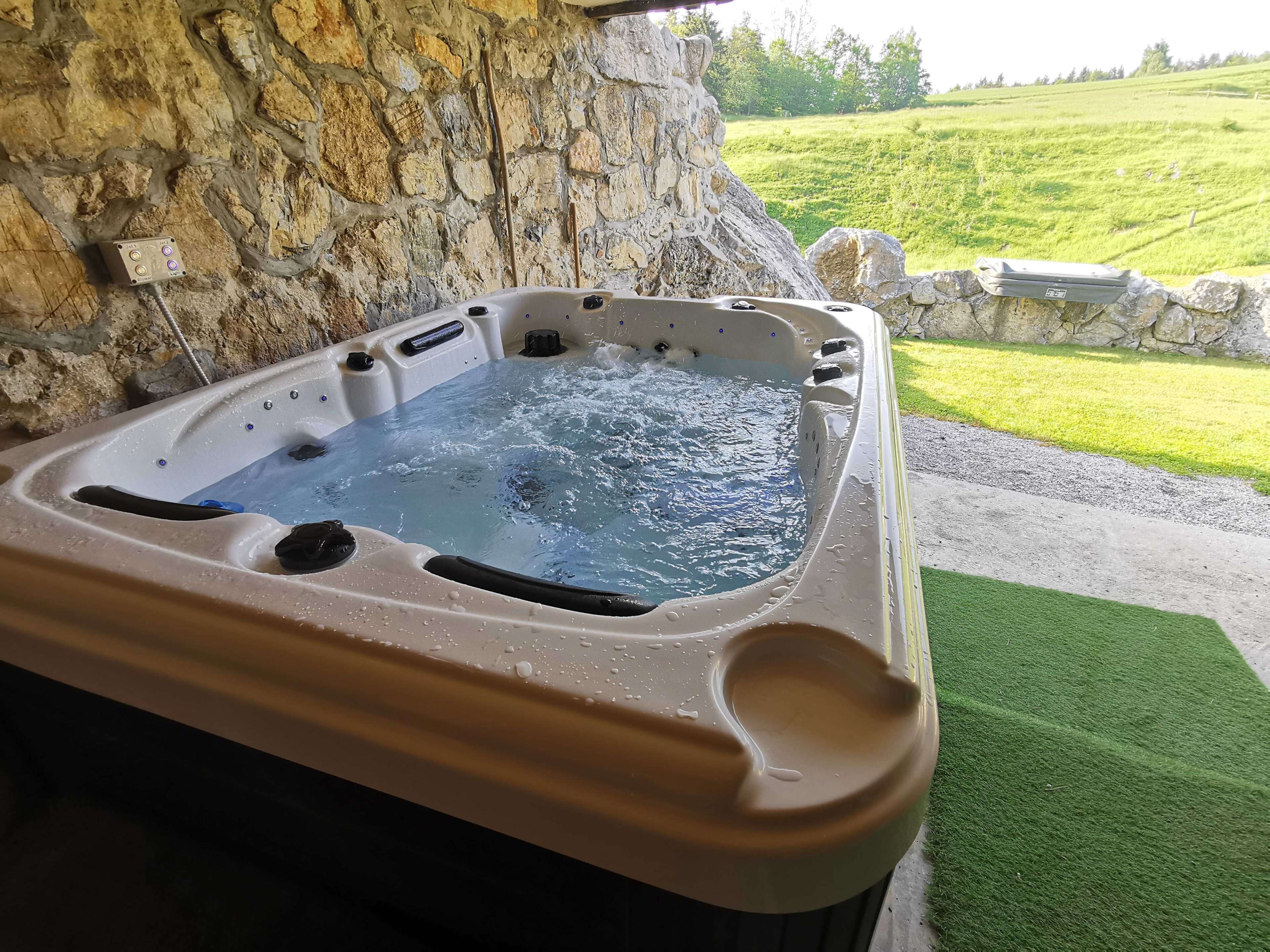 Un jacuzzi con un muro de piedra de fondo, rodeado de césped y un camino de piedras.