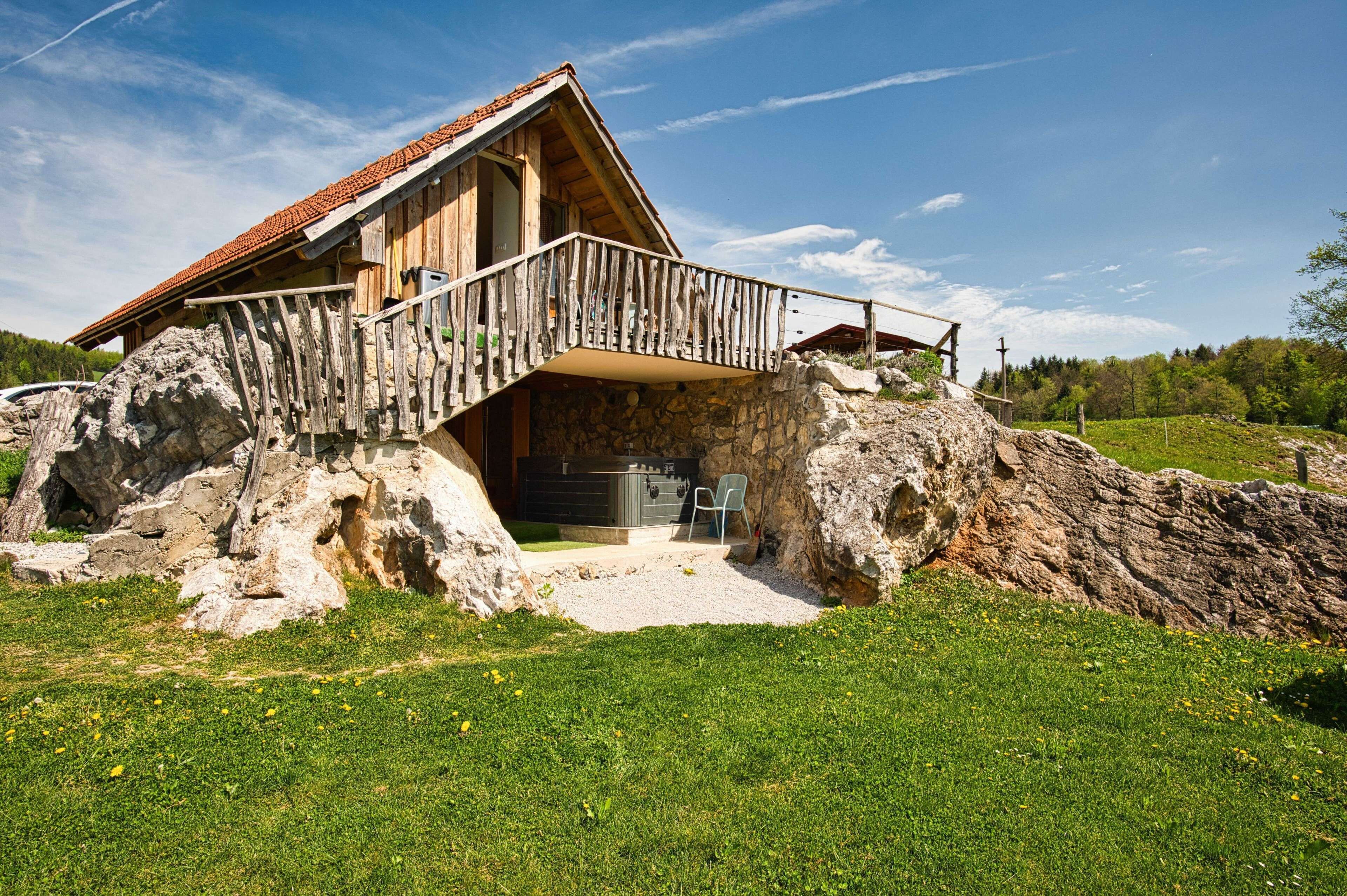 A wooden cabin with a stone foundation, a balcony, and a hot tub.