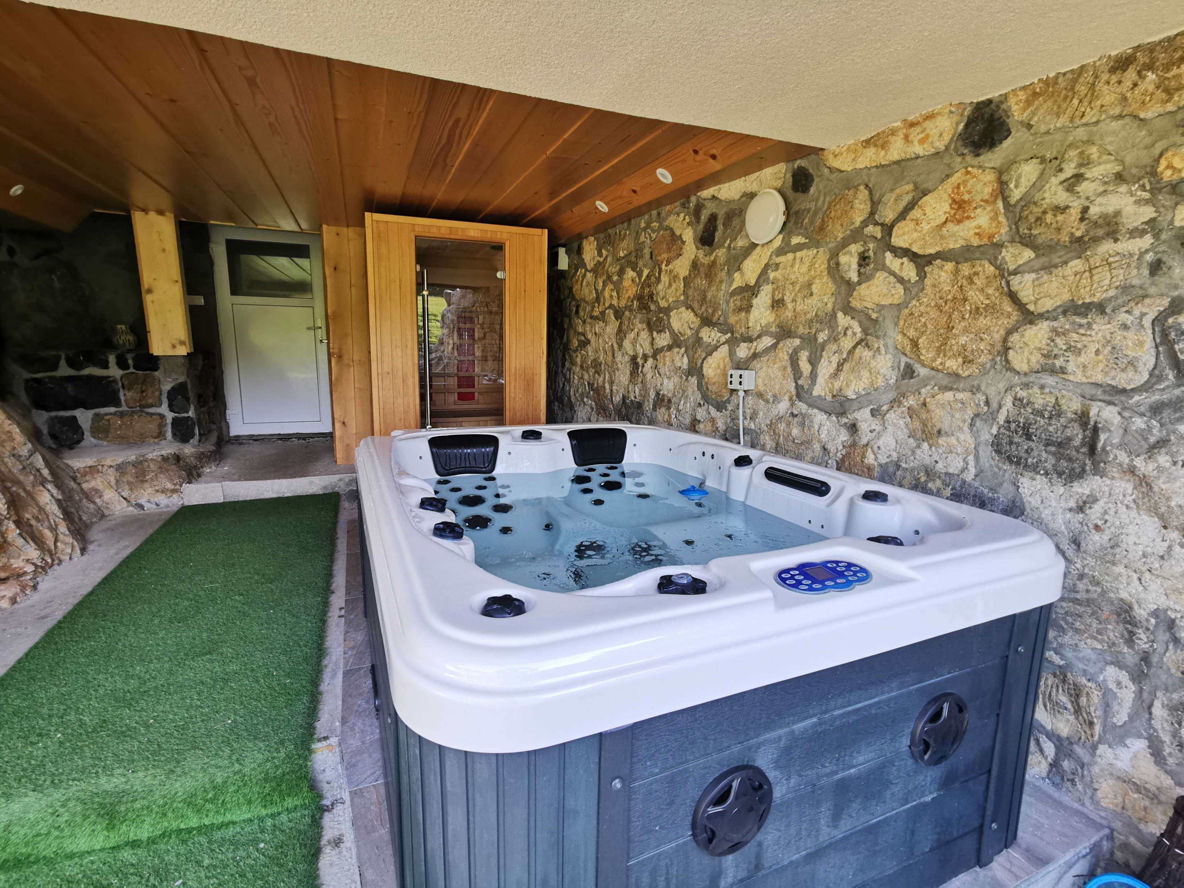 A hot tub with a control panel, surrounded by stone walls and wooden beams.