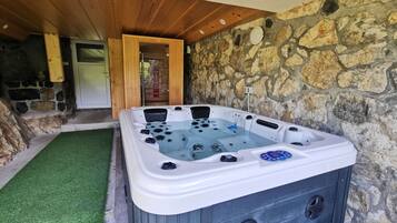 A hot tub with a control panel, surrounded by stone walls and wooden beams.