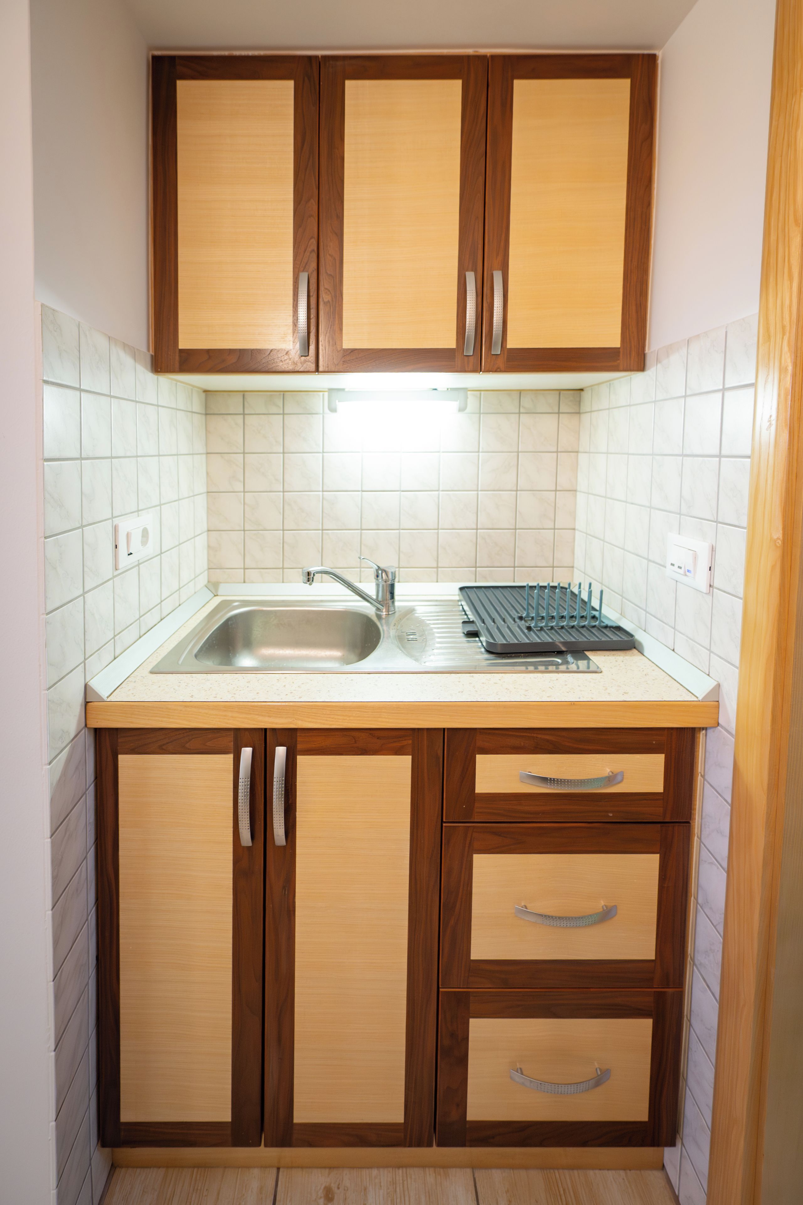A compact kitchen with wooden cabinets, a stainless steel sink, and a built-in drying rack.