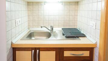 A compact kitchen with wooden cabinets, a stainless steel sink, and a built-in drying rack.