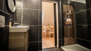 Une salle de bain moderne avec des carreaux noirs, une douche et une table à manger en bois, visible à travers une porte ouverte.