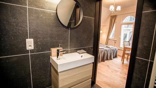 Une salle de bain moderne avec un miroir rond, un lavabo blanc et un meuble-lavabo en bois.