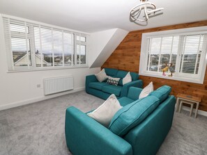 A modern living room with a teal sofa set, white radiator, and large windows with blinds. - Bryn Derw Bach (Moelfre)