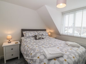 A bedroom with a bed, nightstands, a lamp, and a window with blinds.