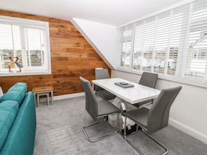 A dining area with a white table and grey chairs, a small stool, and a teal sofa.