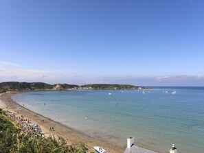 Ein Küstenstrand mit klarem Wasser, Booten und einer hügeligen Landschaft im Hintergrund.