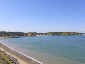A coastal landscape with a sandy beach, calm sea, and hills in the background.