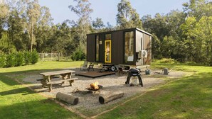 Een compacte, moderne stacaravan met een plat dak, een terras en een vuurkorf in een grasveld.