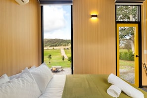 A bedroom with a bed, a view of a grassy landscape through a door, and a small fire pit.