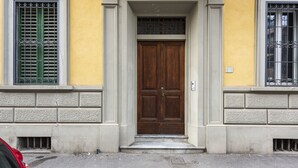 En bygningseingang med en trædobbeltdør, et par trin og et vindue med metalgitter.