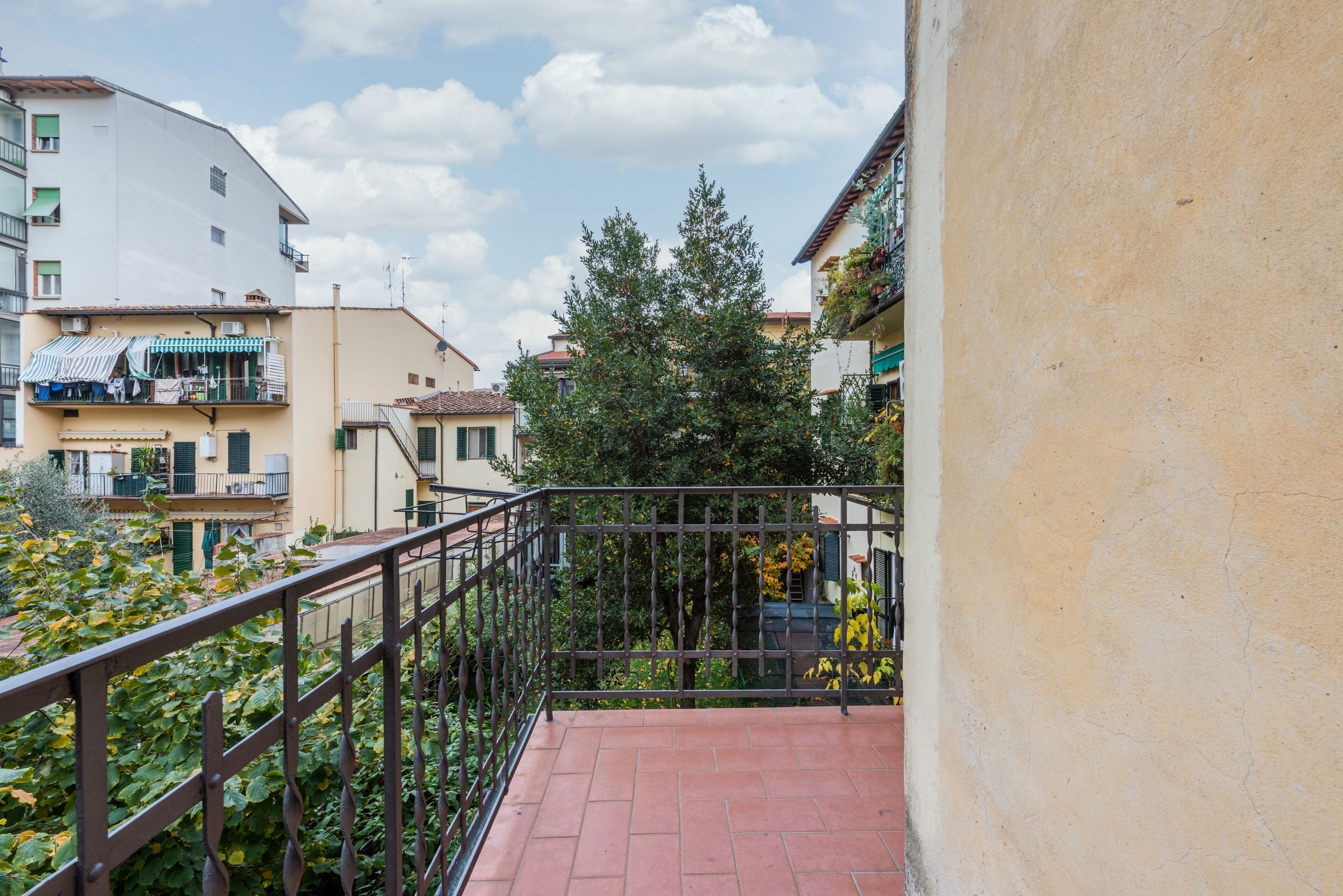 Un balcon doté d’une rambarde en métal donnant sur une cour intérieure agrémentée de plantes et bordée de bâtiments.