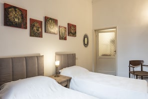 Un dormitorio con dos camas, una mesita de noche con lámpara, una silla y una puerta con mosquitera.