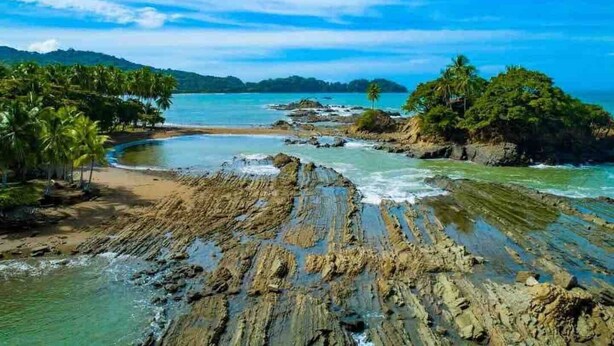 A tropical beach with rocky formations, palm trees, and clear blue waters. - Tranquil Jungle Stay with Breathtaking views, Minutes to Dominical Beach (San Jose Province)
