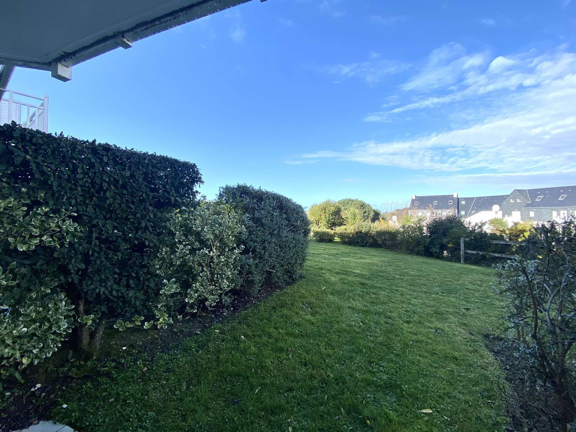 A well-maintained grassy lawn with a neatly trimmed hedge and a clear blue sky.