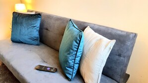 A grey sofa with three pillows in shades of blue and white, and a remote control on the seat. - Salford Ark Comfort Stays Near Trafford Centre (Manchester)