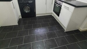 A compact kitchen with white cabinets, a black tiled floor, a washing machine, a microwave, and a stove. - Salford Ark Comfort Stays Near Trafford Centre (Manchester)