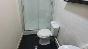 A small bathroom with a toilet, a glass shower enclosure, and a sink. - Salford Ark Comfort Stays Near Trafford Centre (Manchester)