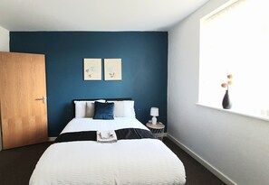 Ein Hotelzimmer mit einem Bett, einem Nachttisch, einer Lampe und zwei gerahmten Bildern an der Wand.