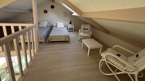 Ein Schlafzimmer mit zwei Betten, einem Sessel, einem kleinen Tisch und einem Balkon mit Geländer.