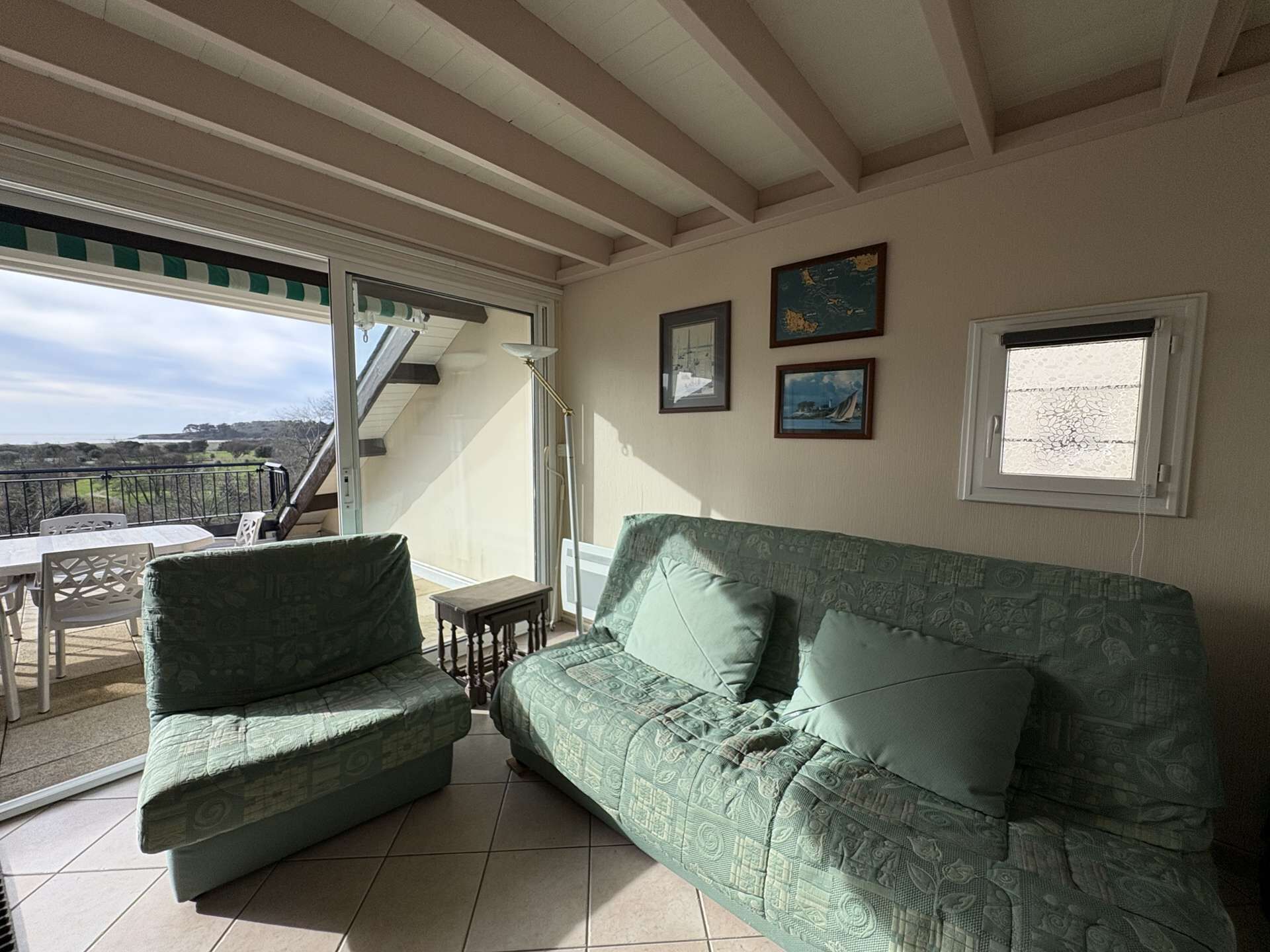 A cozy living room with a green patterned sofa, a small table, and a view of the outdoors.