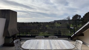 Eine Terrrasse im Freien mit einem runden Tisch und vier Stühlen, mit Blick auf eine malerische Landschaft aus Hügeln und Bäumen.