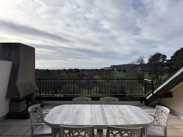 Un patio al aire libre con una mesa redonda y cuatro sillas, con vistas a un paisaje pintoresco con colinas y árboles.