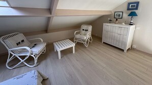 Ein gemütliches Schlafzimmer im Dachgeschoss mit weißen Korbmöbeln, einem kleinen Tisch und einer Kommode.