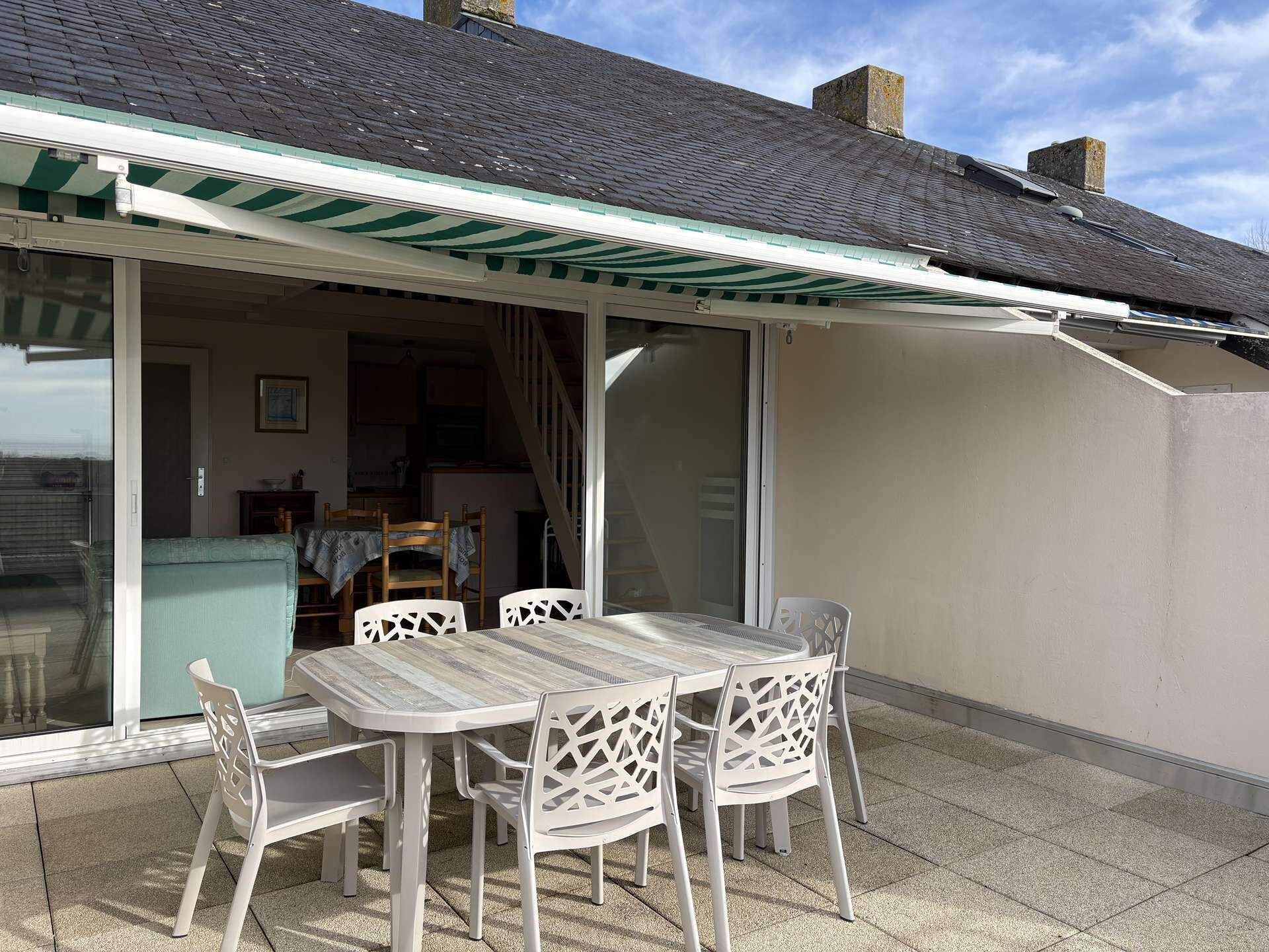 A covered patio with a table and chairs, a sliding glass door leading to an interior space, and a tiled roof.