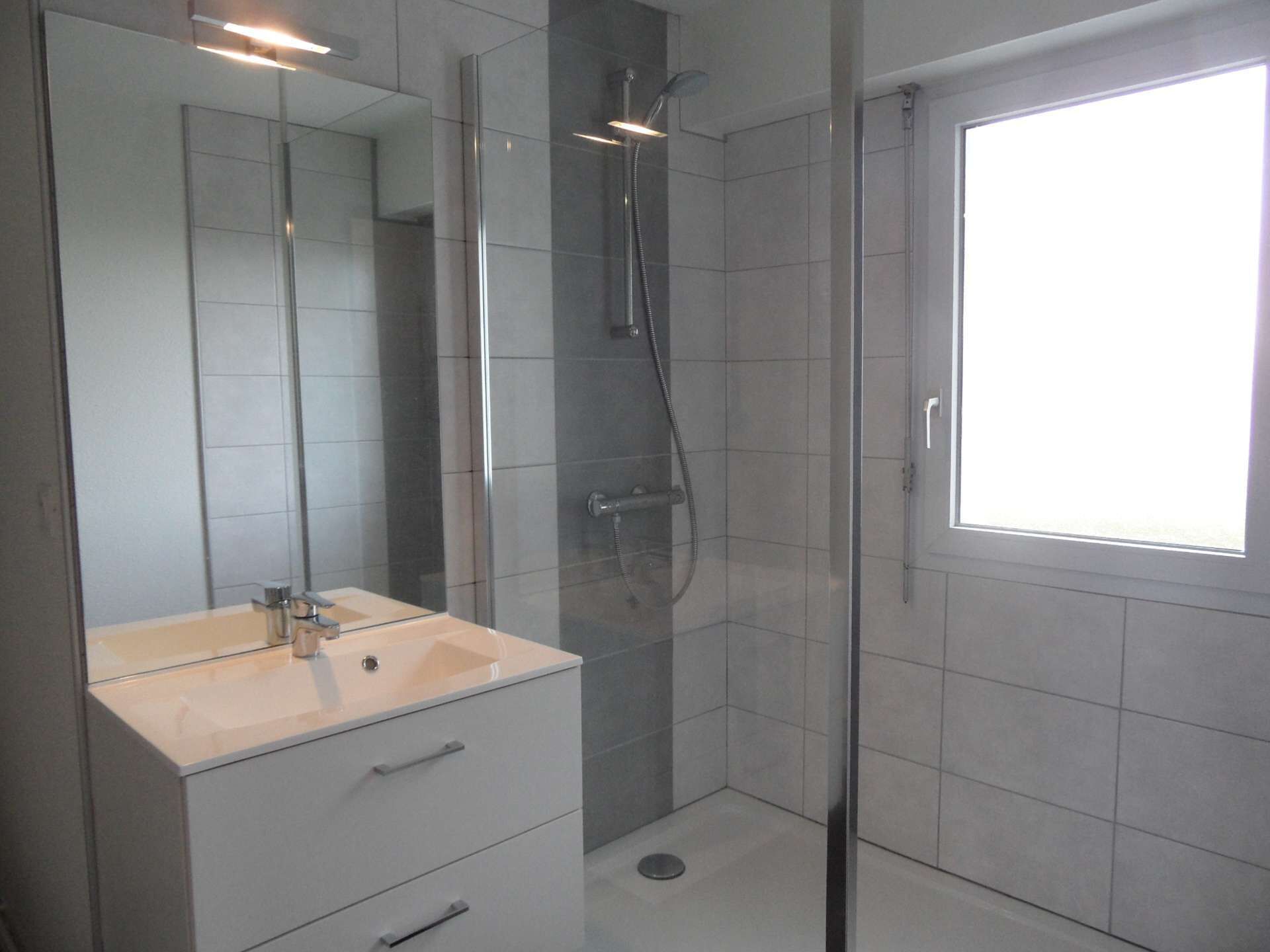 Un baño moderno con cabina de ducha de vidrio, lavamanos blanco y un espejo grande.