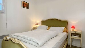 Una cama bien tendida con sábanas blancas, dos lámparas de noche y una mesita de noche con un libro.
