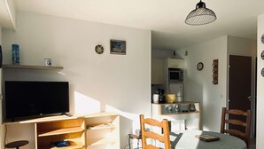 Un espacio habitable pequeño con televisión, muebles de madera, una mesa de comedor con mantel a cuadros y una zona de cocina.