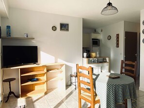 Un espace de vie compact comprenant un téléviseur, des meubles en bois, une table à manger avec une nappe à carreaux et un coin cuisine.
