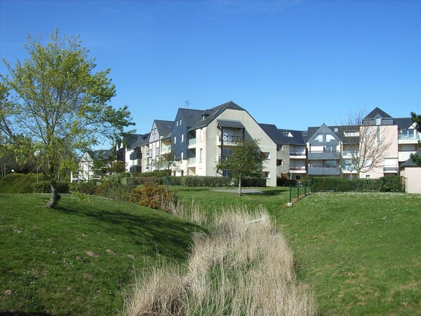 A residential building with multiple balconies, a well-maintained lawn, and a clear blue sky.