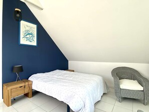 Un dormitorio con una cama, una mesita de noche, una silla y una lámpara de pared.