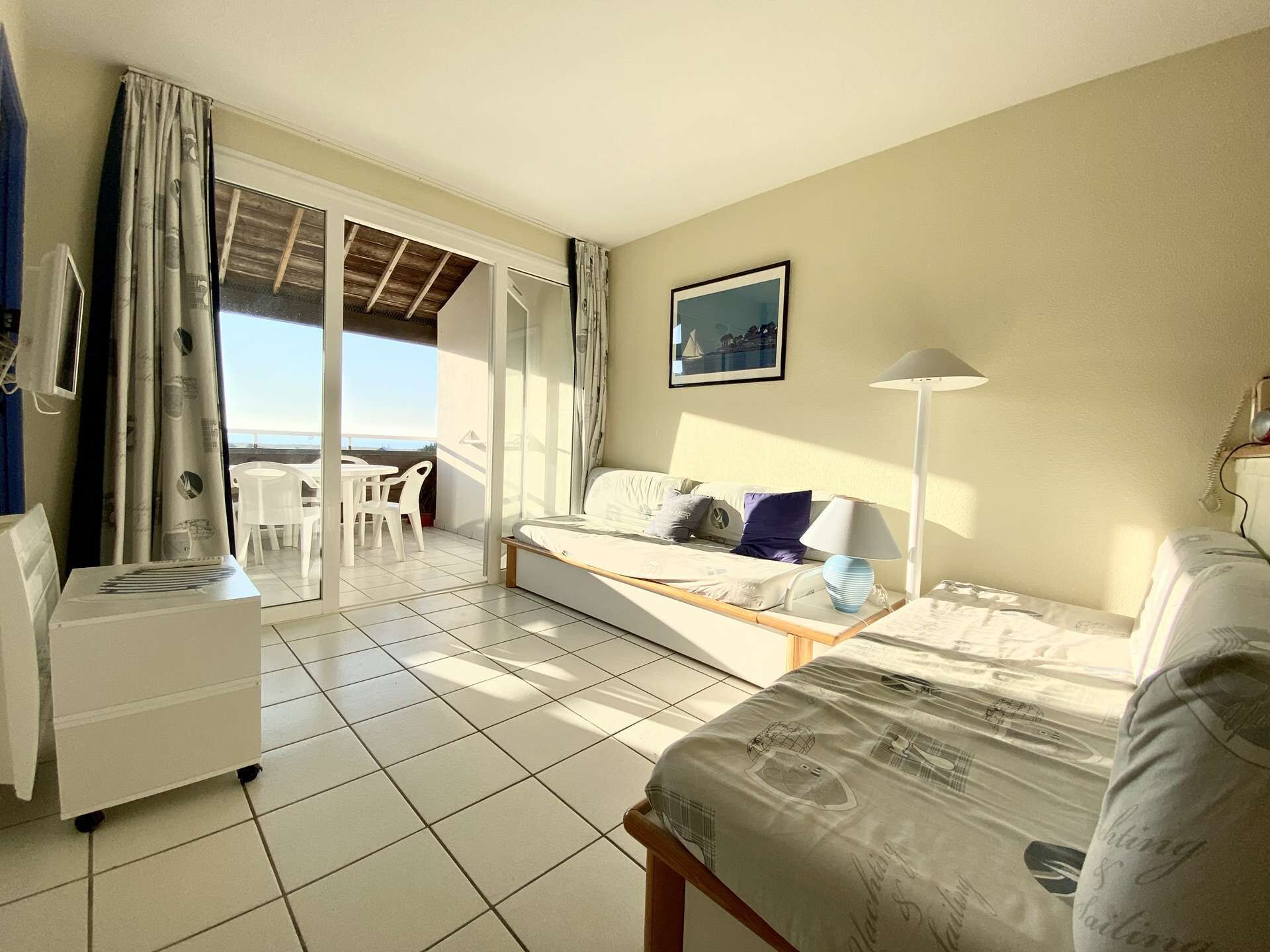 A room with a bed, a desk, a chair, and a view of the sea.