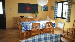 A dining area with a table set for four, surrounded by wooden chairs. A blue and white checkered sofa is in the foreground.